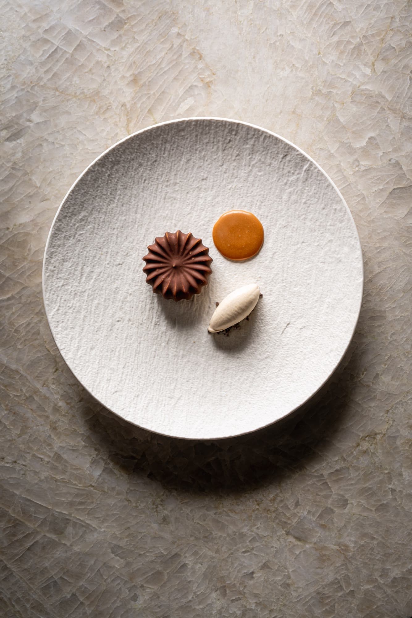 Chocolate dessert with a dot of caramel and a quenelle on a textured white plate